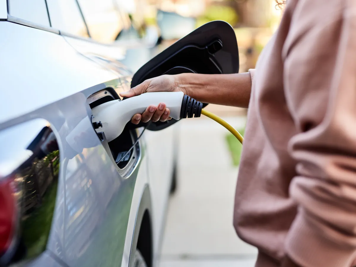Pessoa conectando carregador elétrico amarelo em carro branco, representando lei carregadores condomínios São Paulo e nova infraestrutura predial para veículos elétricos