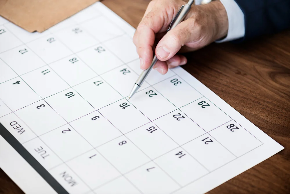 Mão masculina com caneta apontando para calendário mensal na gestão condominial, simbolizando planejamento anual estruturado para síndicos