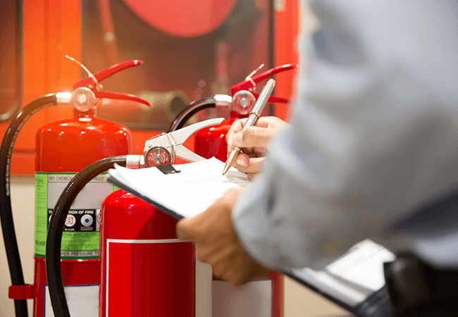Inspetor profissional verificando extintores de incêndio vermelhos com prancheta, demonstrando manutenção preventiva para brigada de incêndio em condomínios